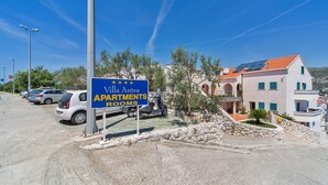 A sign for Villa Antea apartments with a clear view of parked cars and a building with a red-tiled roof.