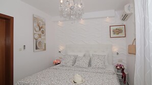Un dormitorio con una colcha estampada, un candelabro, aire acondicionado montado en la pared y un cuadro enmarcado.
