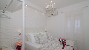A neatly arranged bedroom with a bed, a chandelier, an air conditioning unit, and a window with sheer curtains.