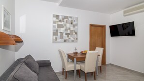Ein modernes Wohnzimmer mit einem grauen Sofa, einem Esstisch mit Stühlen, einer Holztür und einem Flachbildfernseher an der Wand.