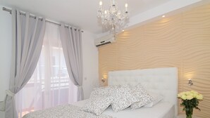 Ein Schlafzimmer mit Bett, Vorhängen, einer Deckenleuchte, einer Wand-Klimaanlage und einem kleinen runden Tisch mit Blumen in einer Vase.