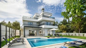 Una casa moderna de dos pisos con piscina, mobiliario exterior y un jardín bien cuidado.