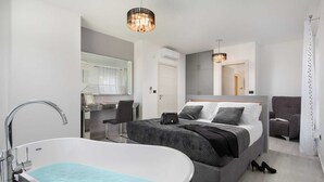 Una habitación de hotel moderna con una cama grande, una tocador independiente con espejo, una bañera y dos lámparas colgantes.
