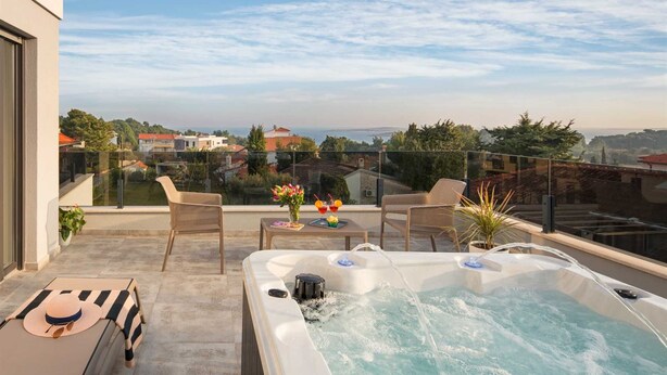 Una terraza en la azotea con un jacuzzi, dos sillas de mimbre, una mesa con bebidas y vistas a la ciudad.