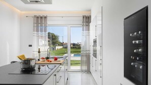 Una cocina moderna con una isla central, horno empotrado y vistas a una piscina y zonas verdes.