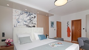 Ein modernes Hotelzimmer mit einem großen Bett, einem Nachttisch mit Blumenstrauß, einer Zeitschrift auf dem Bett und einer Holztür.