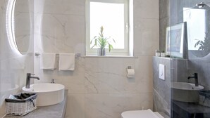 Ein modernes Badezimmer mit rundem Spiegel, Fenster, Toilette und Waschbecken.
