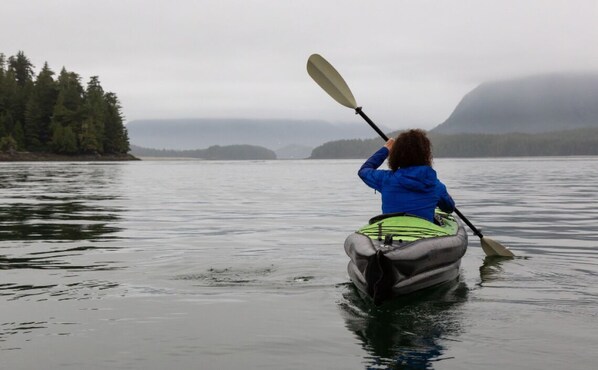 Une personne fait du kayak sur un lac paisible, avec une zone boisée sur la gauche et une montagne en arrière-plan.