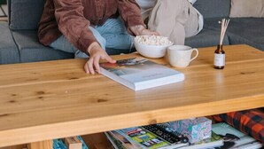 Un salon comprenant un canapé, une table basse avec des livres et un bol de pop-corn, ainsi qu’une bibliothèque remplie de divers objets.