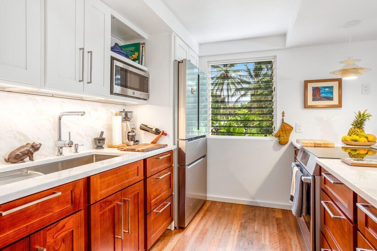 Una cocina moderna con armarios blancos, un refrigerador de acero inoxidable y un ventanal con vistas a zonas verdes.