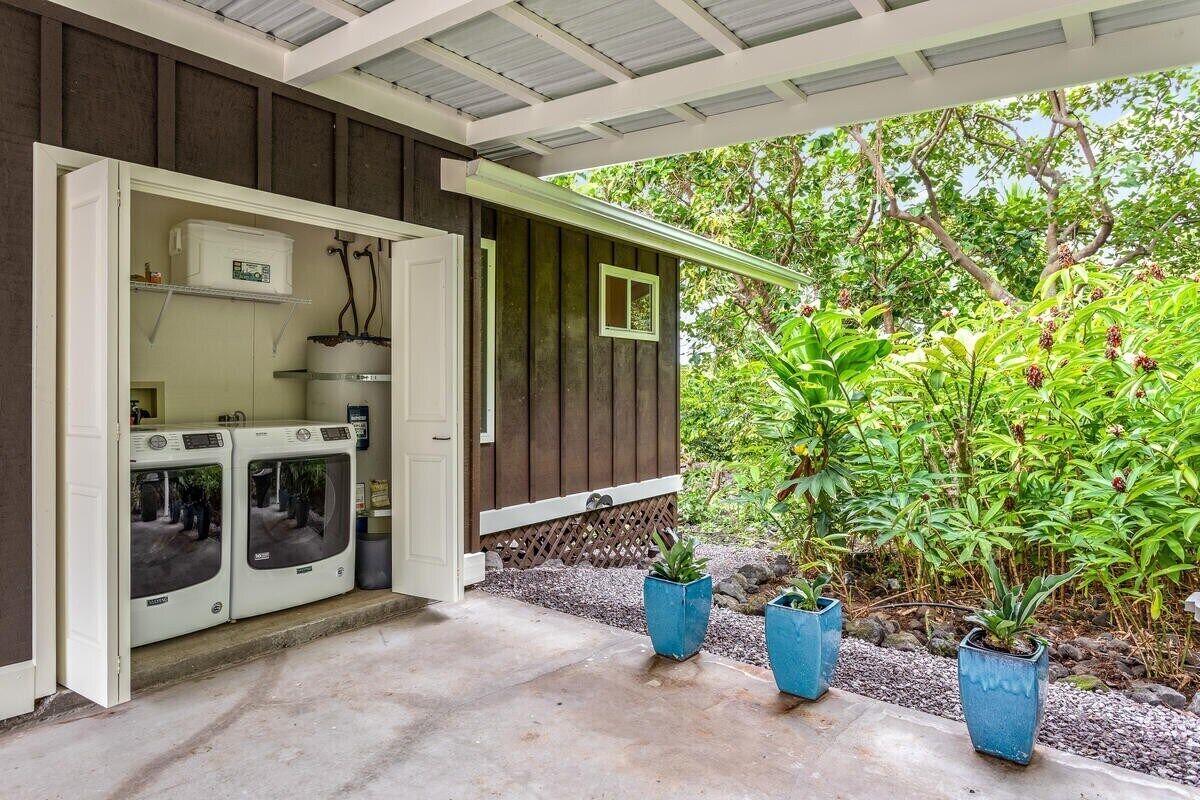 A laundry room with two washing machines and a drying machine, a wooden exterior, and a garden area with potted plants.