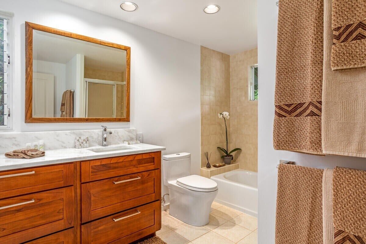 A modern bathroom with a wooden vanity, a large mirror, a toilet, and a bathtub.