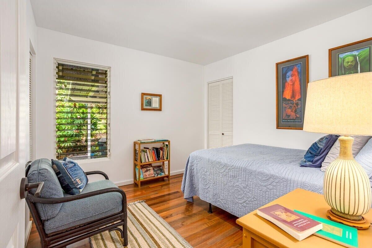 A bedroom with a bed, a chair, a bookshelf, and a window with blinds.