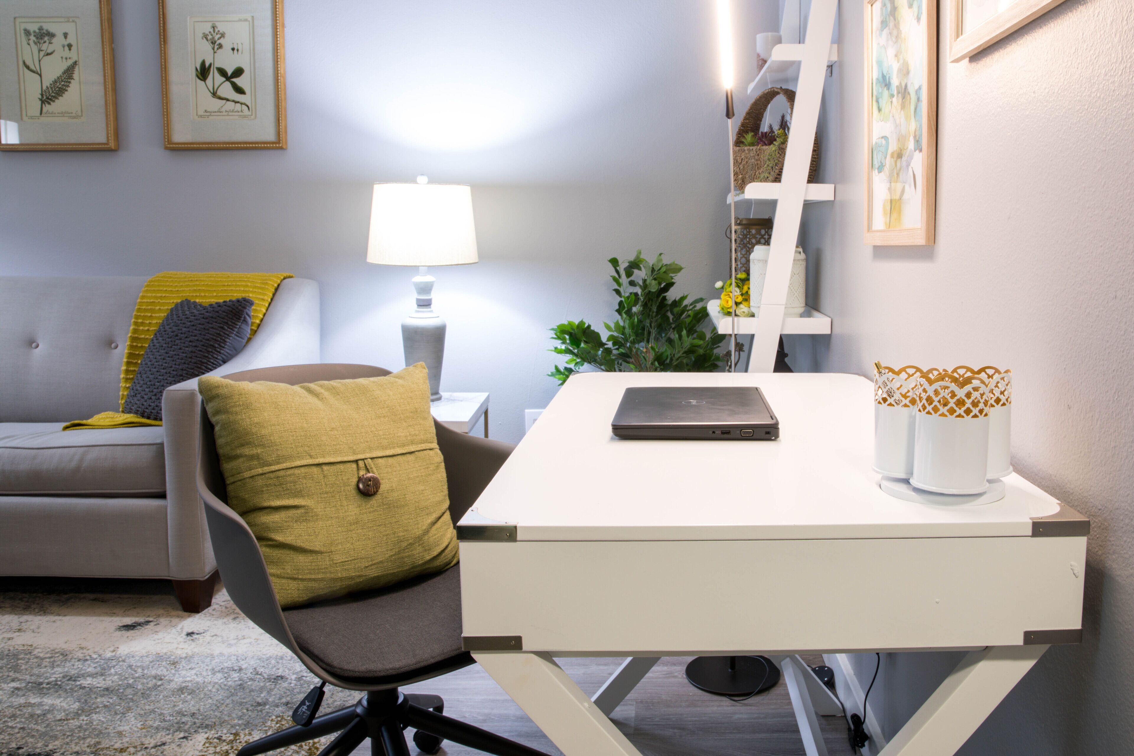 Un espace de bureau moderne avec un bureau blanc, un ordinateur portable, une lampe et une plante.