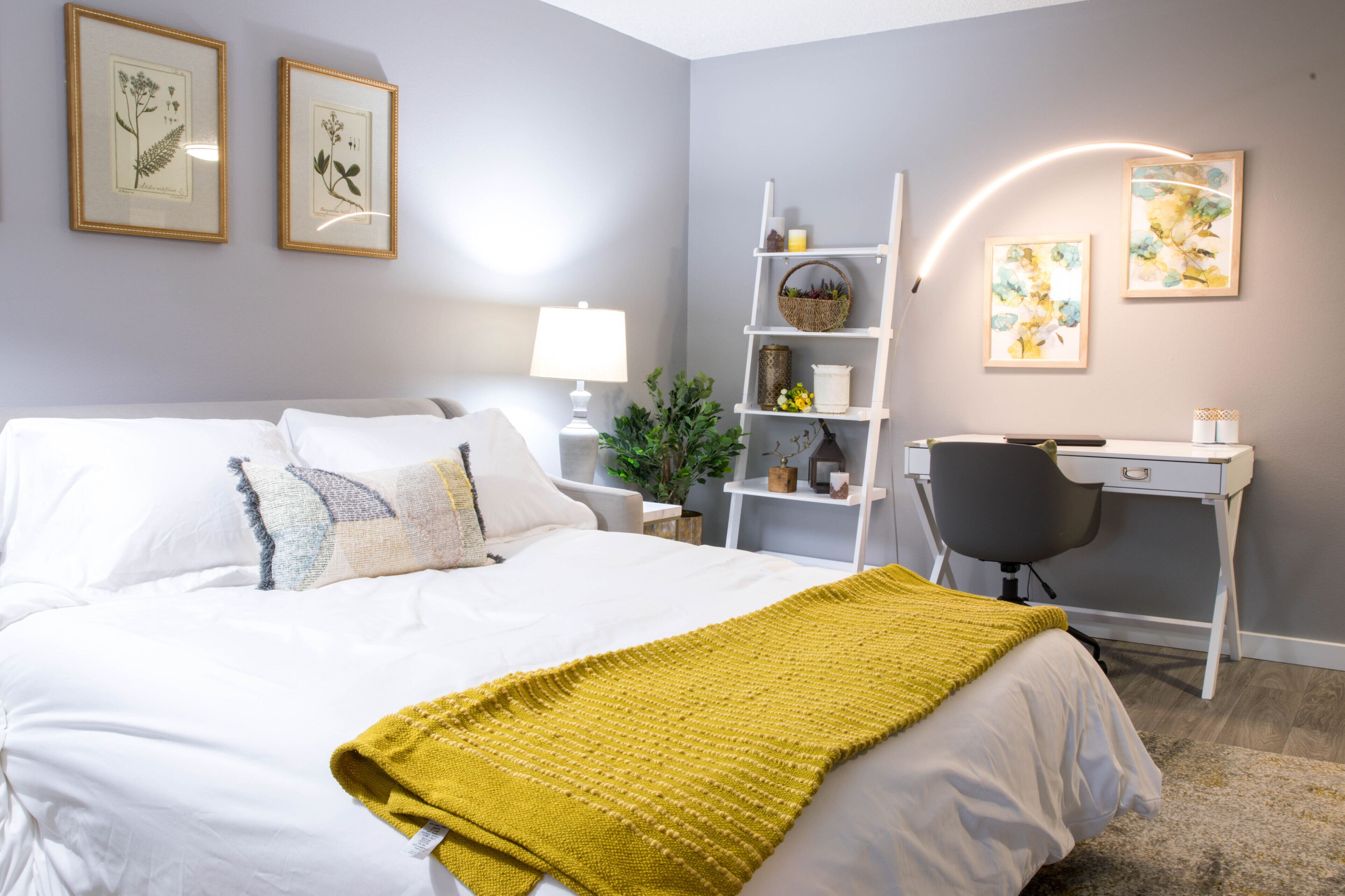 Een netjes ingerichte slaapkamer met een bed, nachtkastje, lamp en een bureau met stoel.