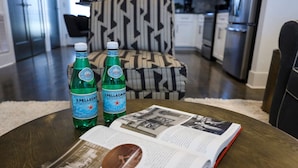Un libro abierto sobre una mesa con dos botellas de S. Pellegrino y un cojín estampado en una cocina moderna.