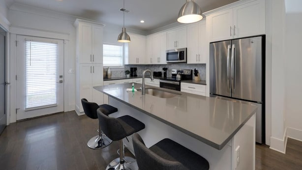Una cocina moderna con armarios blancos, electrodomésticos de acero inoxidable y una isla central con taburetes de bar.