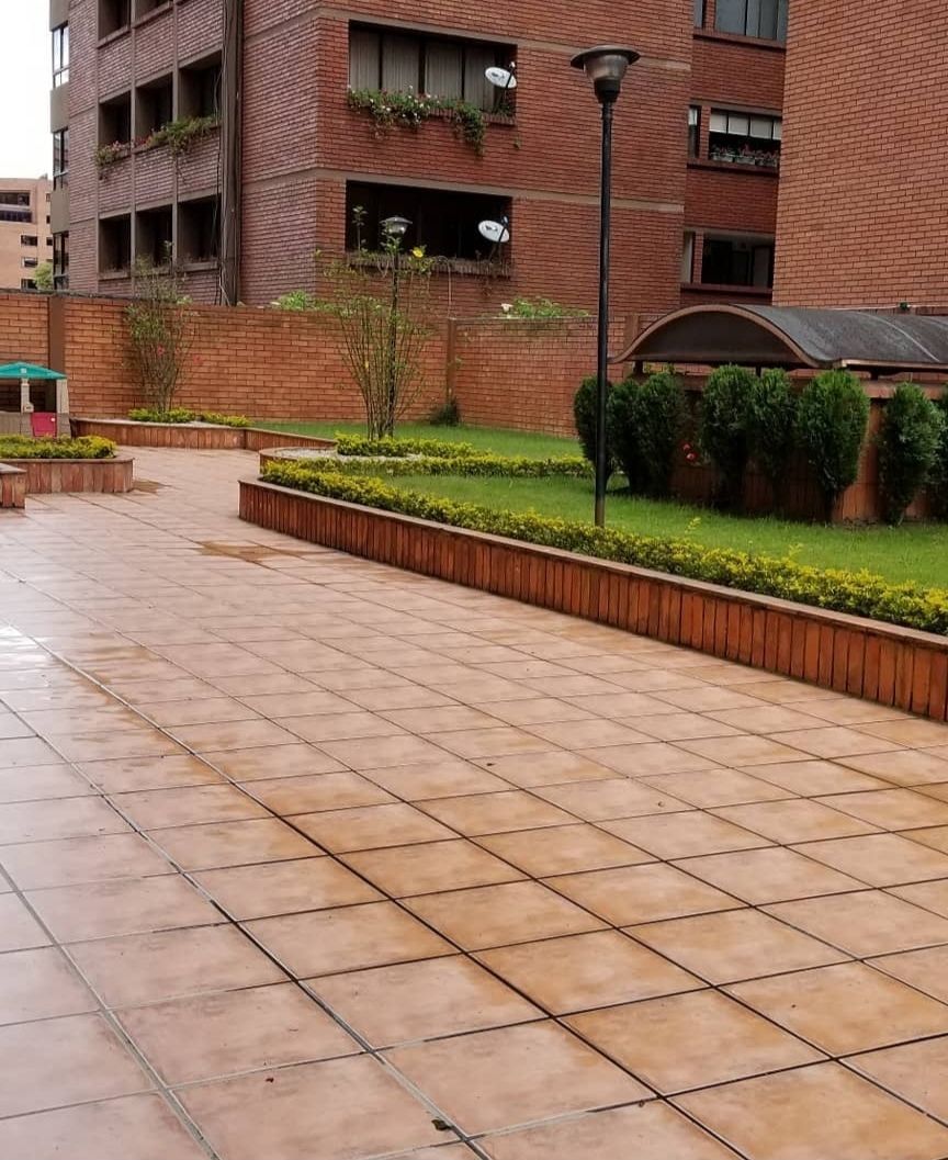 A paved walkway with a brick building in the background, a lamp post, and a small garden area.