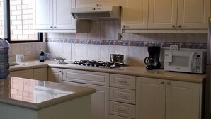 Een keuken met een gasfornuis, magnetron en koffiezetapparaat. Er is een betegelde spatwand en lichte kastjes.