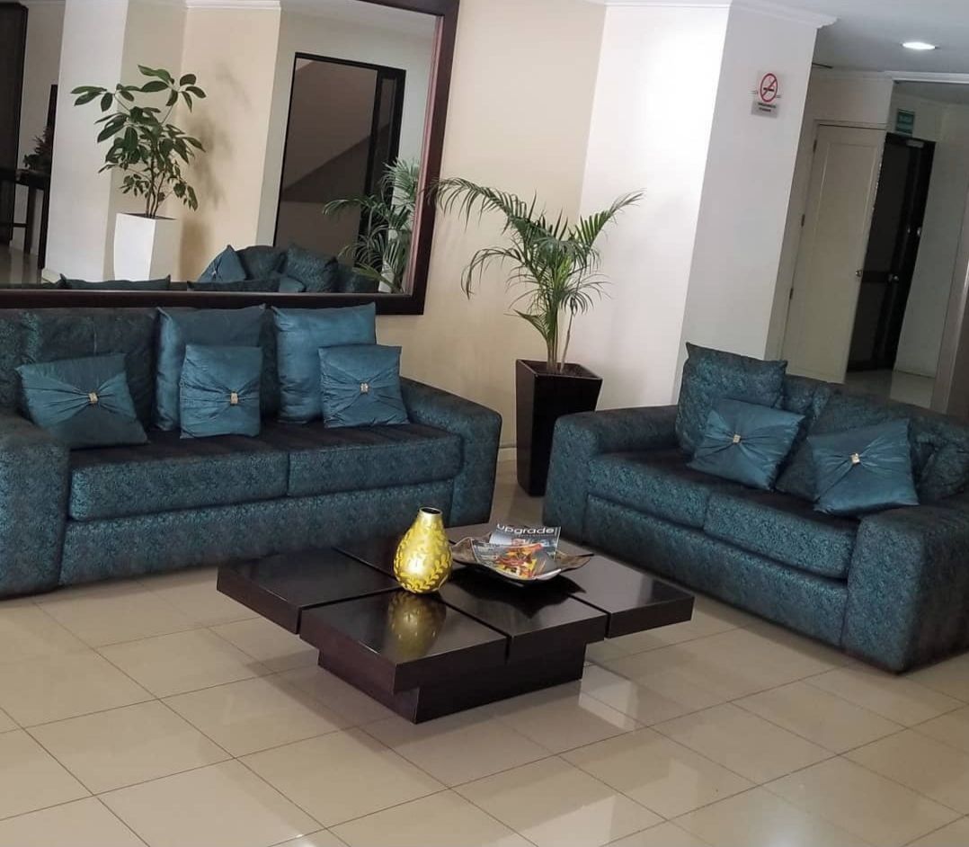 A hotel lobby with two sofas, a coffee table, a large mirror, and potted plants.
