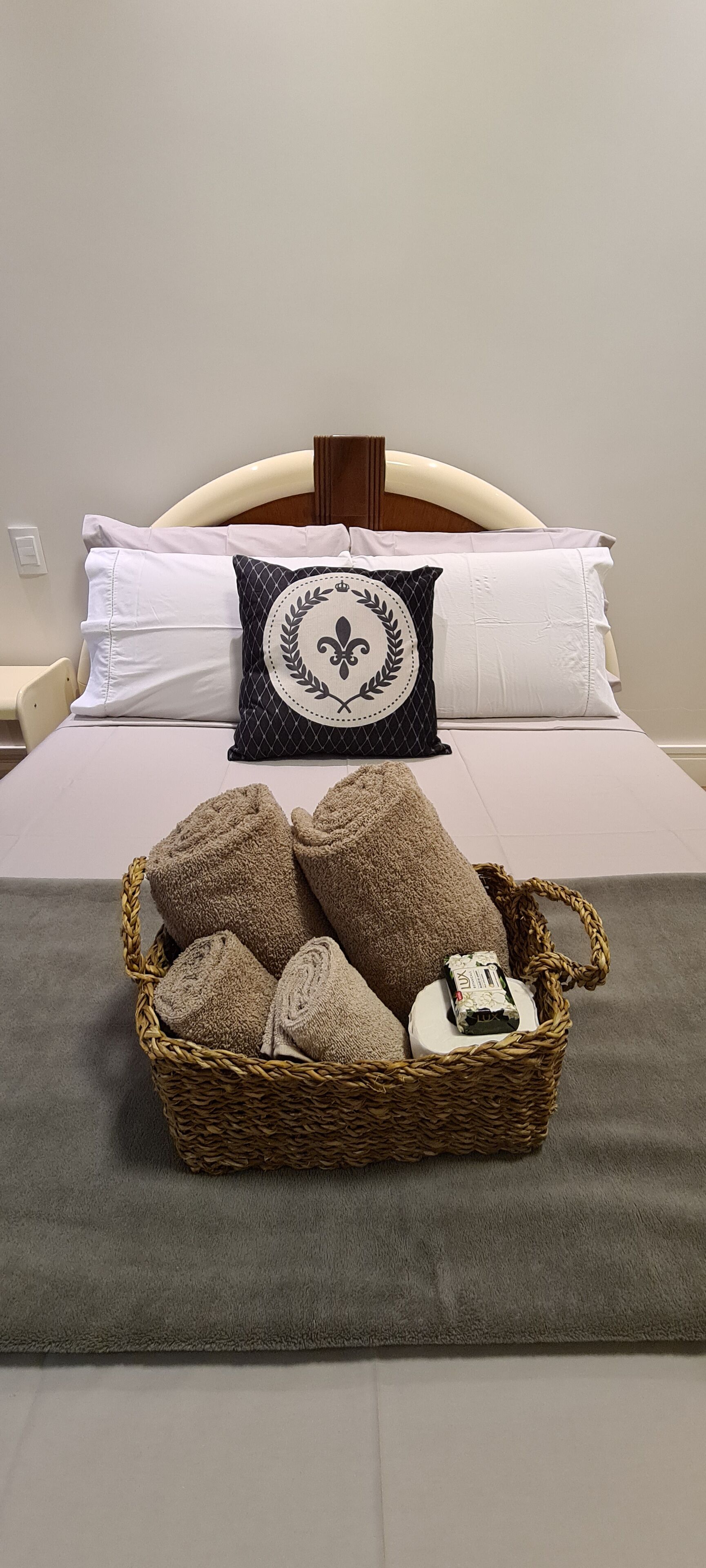 Un lit bien fait, avec une tête de lit, des oreillers et un panier rempli de serviettes enroulées.