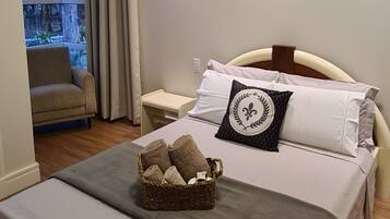 Une chambre à coucher avec un grand lit, une table de chevet, une commode, une fenêtre avec des rideaux et une vue sur les arbres à l’extérieur.
