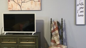 Een woonkamer met een televisie op een kast, een stoel, een kunstwerk aan de muur en een decoratief bord.