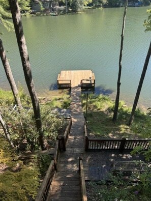A wooden dock leading to a small wooden platform with benches, surrounded by trees and a calm lake.