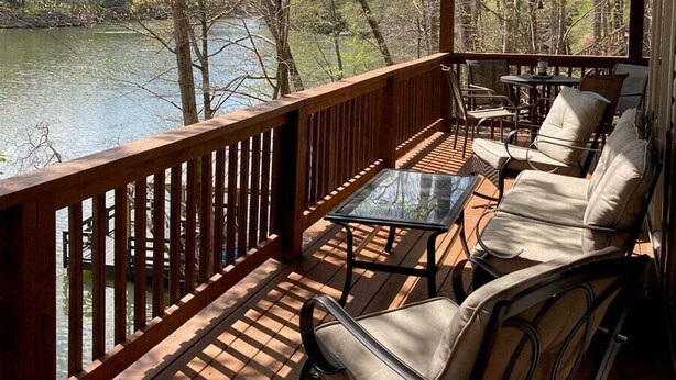 A wooden deck with a glass table and chairs overlooking a lake. - Lakeside at Rumbling Bald (Lake Lure)