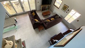 A living room with a brown sofa, a TV, and a wooden coffee table. There is a sliding glass door leading to an outdoor area.