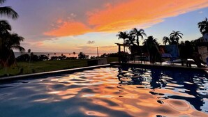 A swimming pool with a sunset view, palm trees, and a clear sky.