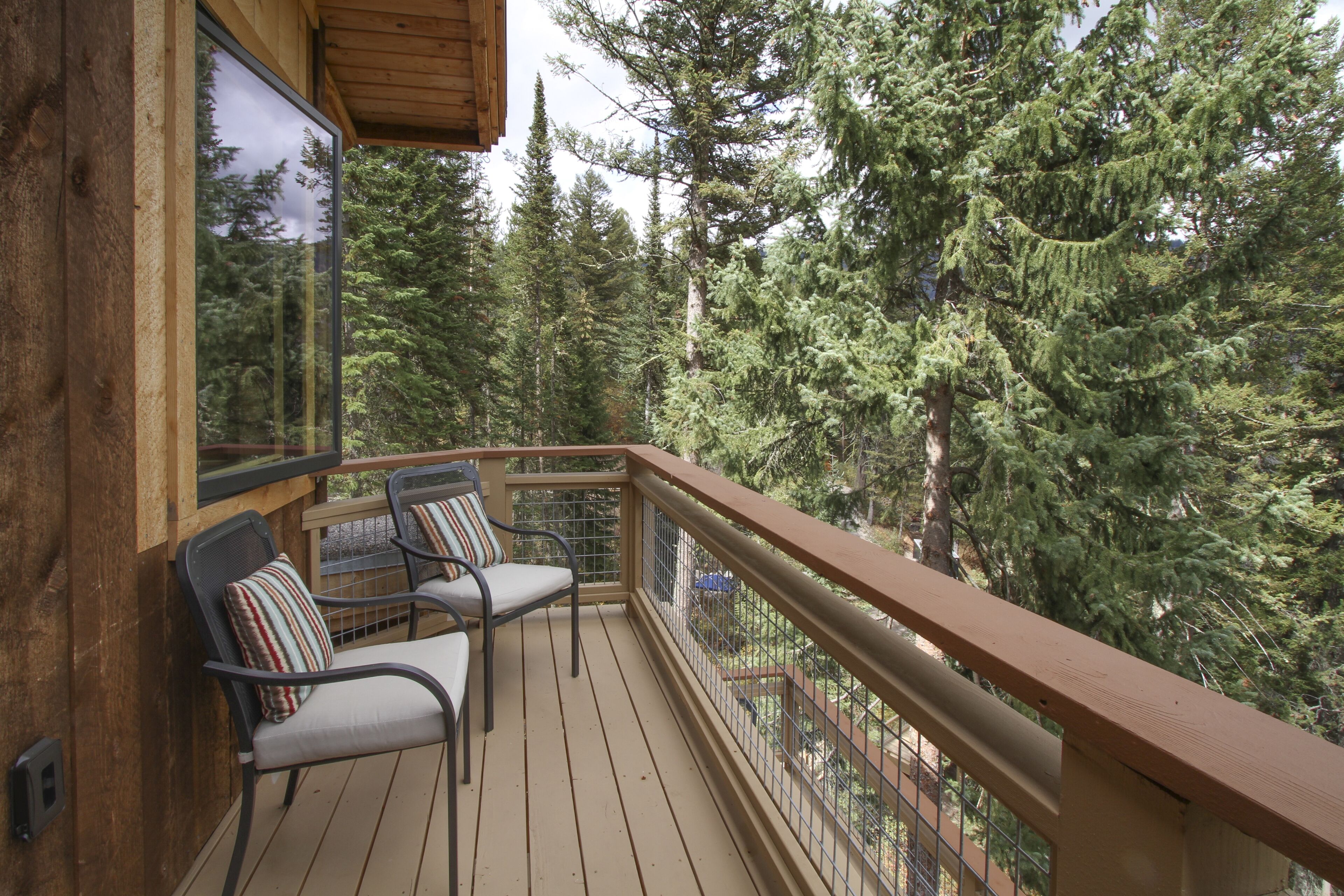 Une terrasse en bois avec deux chaises et une rambarde, donnant sur une zone boisée.