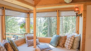 A cozy cabin interior with a wooden bench, cushioned seating, and large windows offering a forest view. - Jackson Hole Hideout Entire Home, Perfect for a Micro Wedding, Corporate Retreat (Wilson)