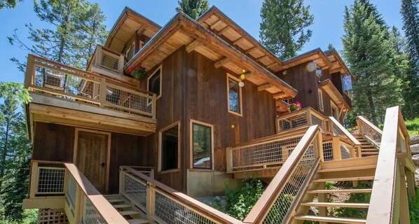 A multi-level wooden cabin with balconies, a staircase, and a natural forest backdrop. - Jackson Hole Hideout Entire Home, Perfect for a Micro Wedding, Corporate Retreat (Wilson)