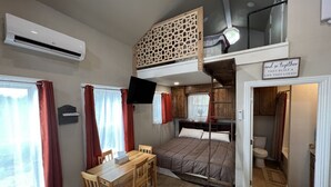 Et lille værelse med køjeseng, spiseplads med bord og stole, et TV ophængt på væggen og et skilt over døren.