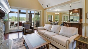 Ein geräumiges Wohnzimmer mit einer großen Couch, einem Couchtisch und einem Kamin. Ein Balkon bietet Blick auf die Berge.