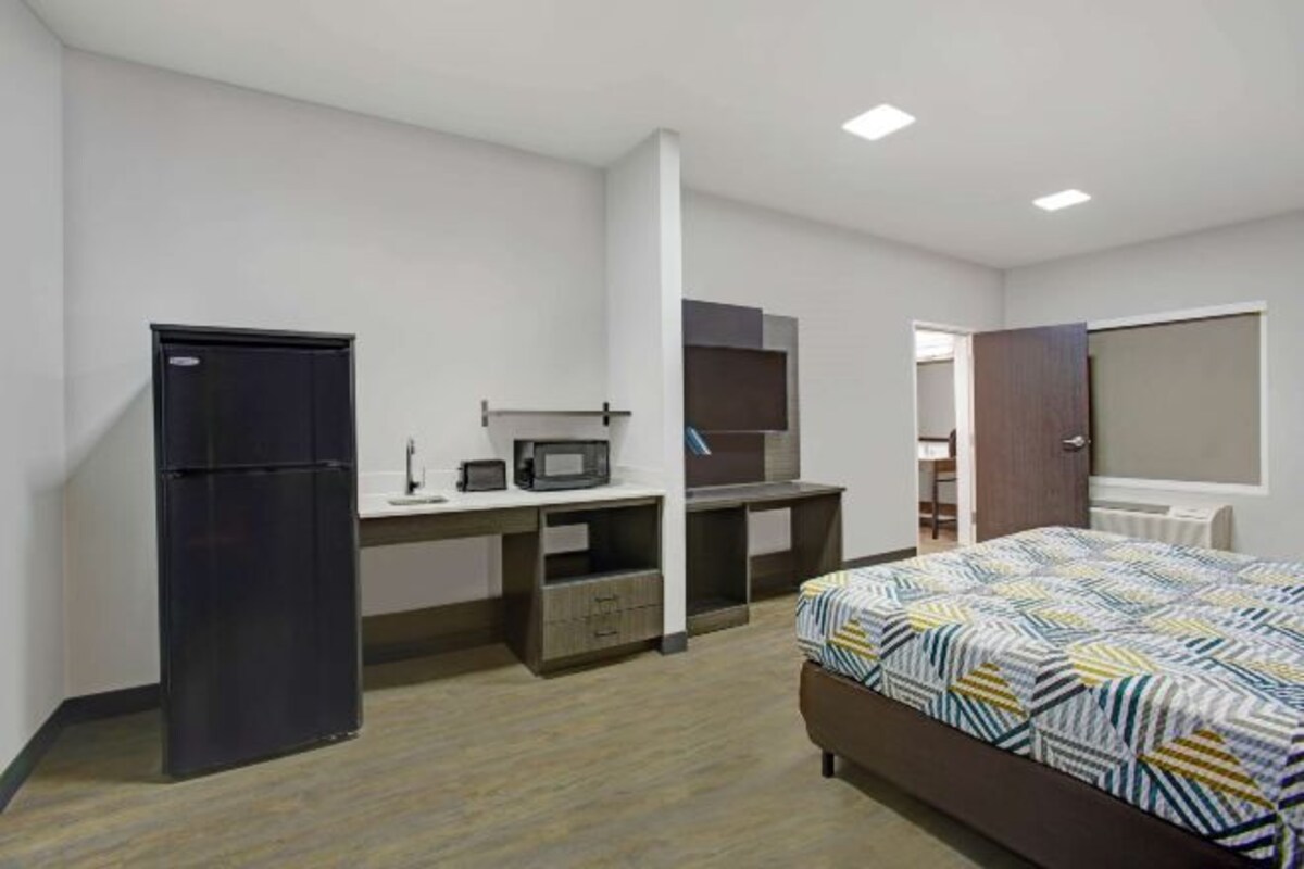 A bedroom with a bed, a desk, a refrigerator, and a microwave.