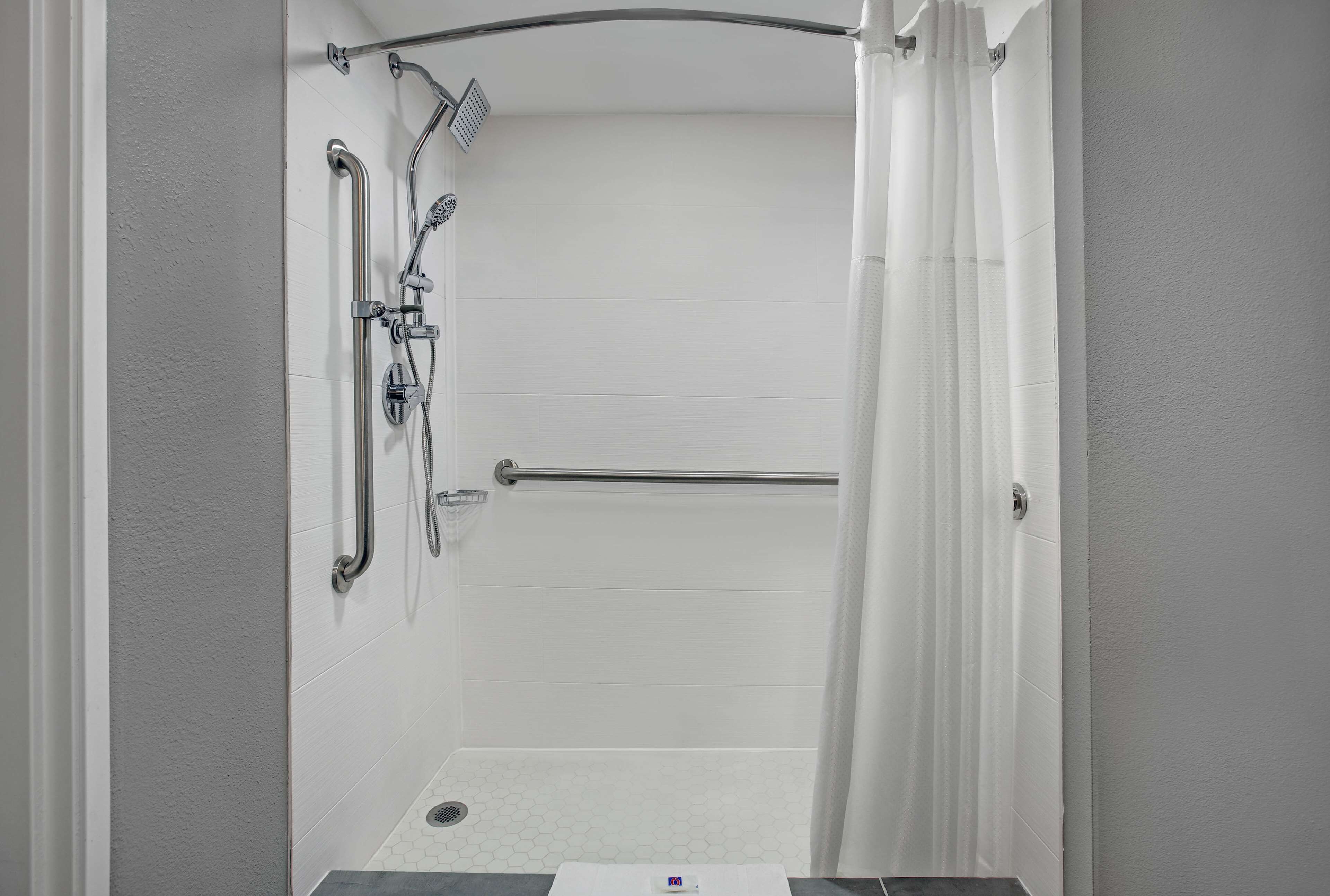 A walk-in shower with a handrail, a showerhead, and a towel rack.