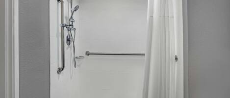 A walk-in shower with a handrail, a showerhead, and a towel rack.