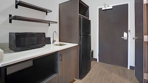 A compact kitchen with a microwave, sink, and dark wooden cabinets. - Motel 6 Monahans, TX (Monahans)