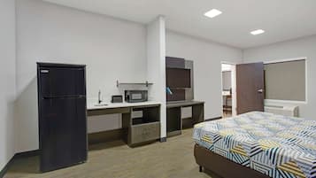 A bedroom with a bed, a desk with a computer, a microwave, and a refrigerator.