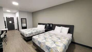 A hotel room with two beds, a desk, and a mirror.