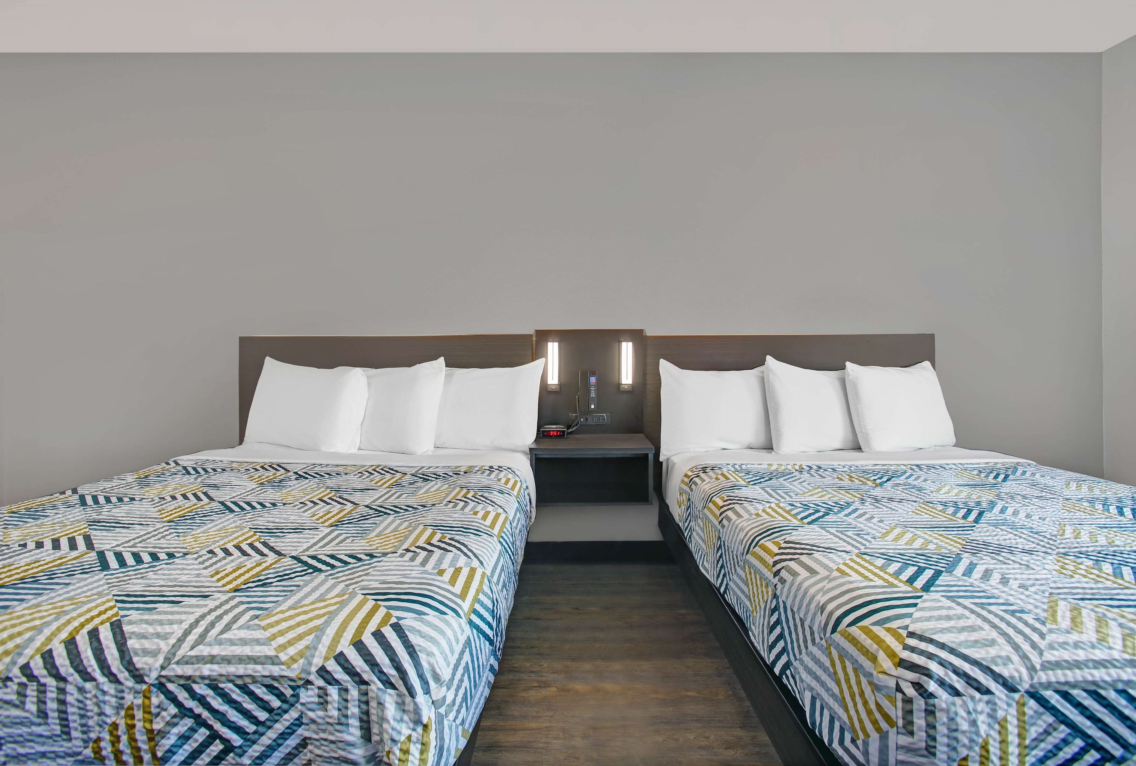 Una habitación de hotel con dos camas individuales, una mesita de noche con lámpara y una pequeña mesa entre las camas.