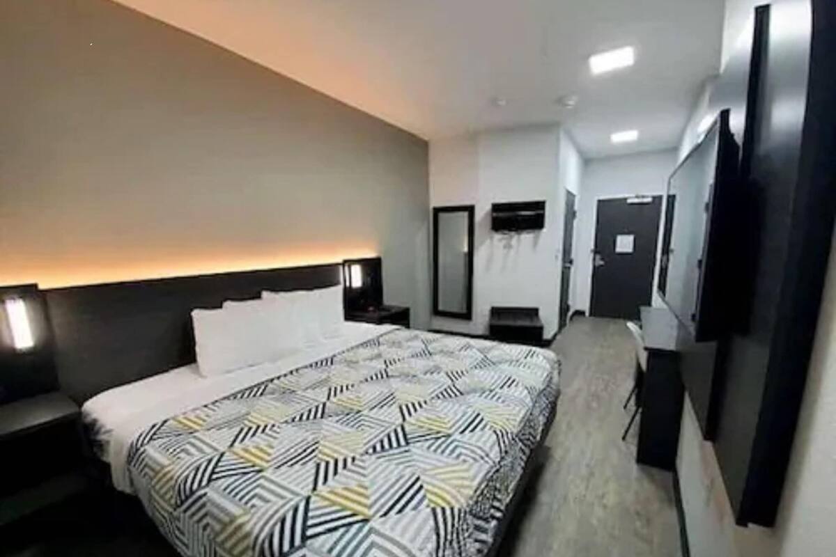 Une chambre d’hôtel moderne dotée d’un grand lit, de tables de chevet, d’un téléviseur à écran plat, d ’un miroir et d’une porte.