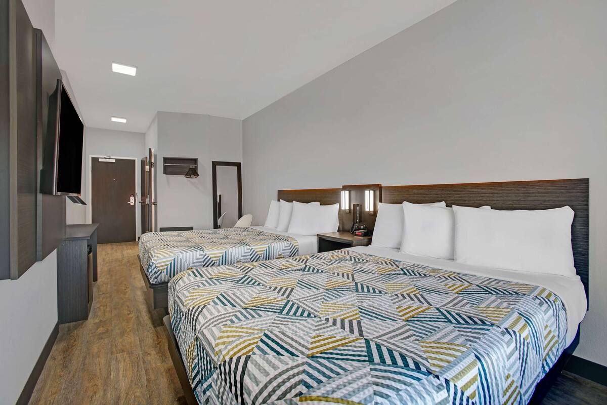 Une chambre d’hôtel avec deux lits, une télévision, un bureau et une porte donnant sur une autre chambre.