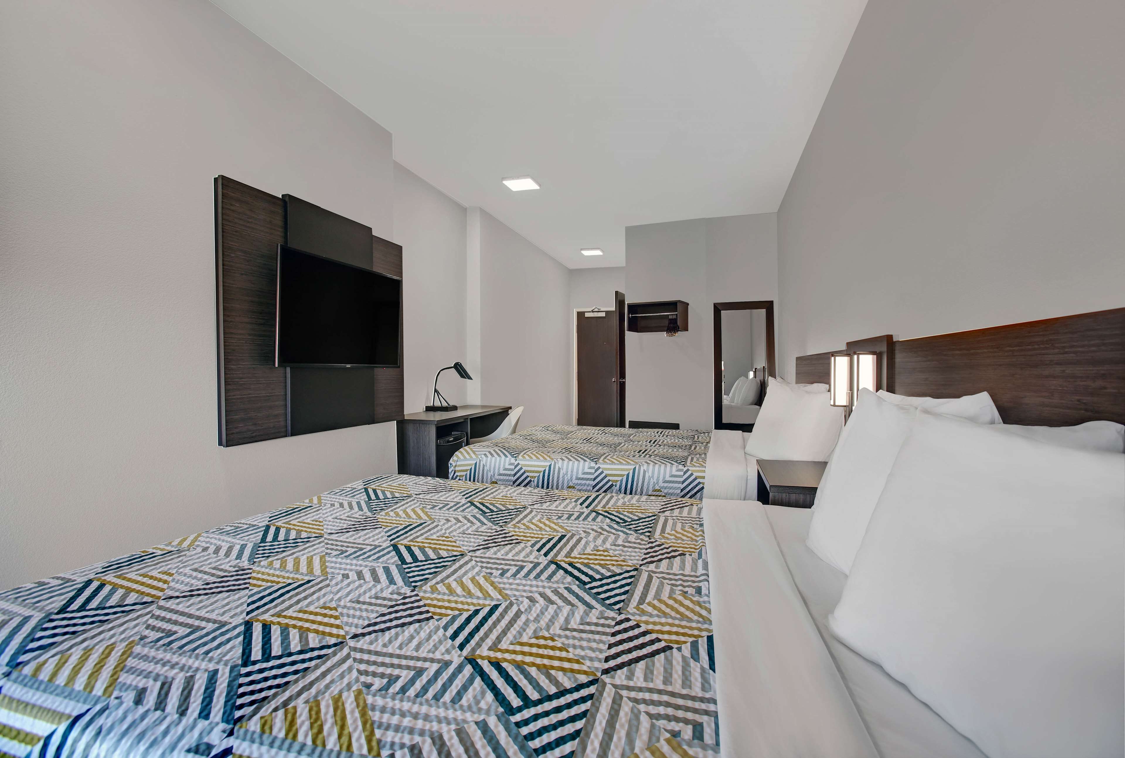 Habitación de hotel con dos camas, televisión, escritorio y espejo.