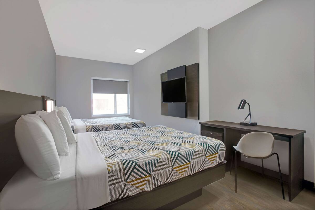 Une chambre moderne avec un lit, un bureau et une chaise. On y trouve une fenêtre et un téléviseur à écran plat fixé au mur.