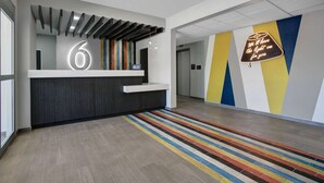 A modern reception area with a digital display, a reception desk, and a colorful striped carpet. - Motel 6 Monahans, TX (Monahans)