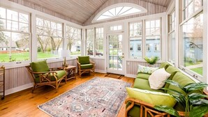 A sunroom with wooden floors, green cushioned seating, and large windows offering a view of the outdoors.