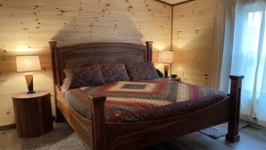 Quarto com painéis de madeira, uma cama, duas mesas de cabeceira e luminárias.